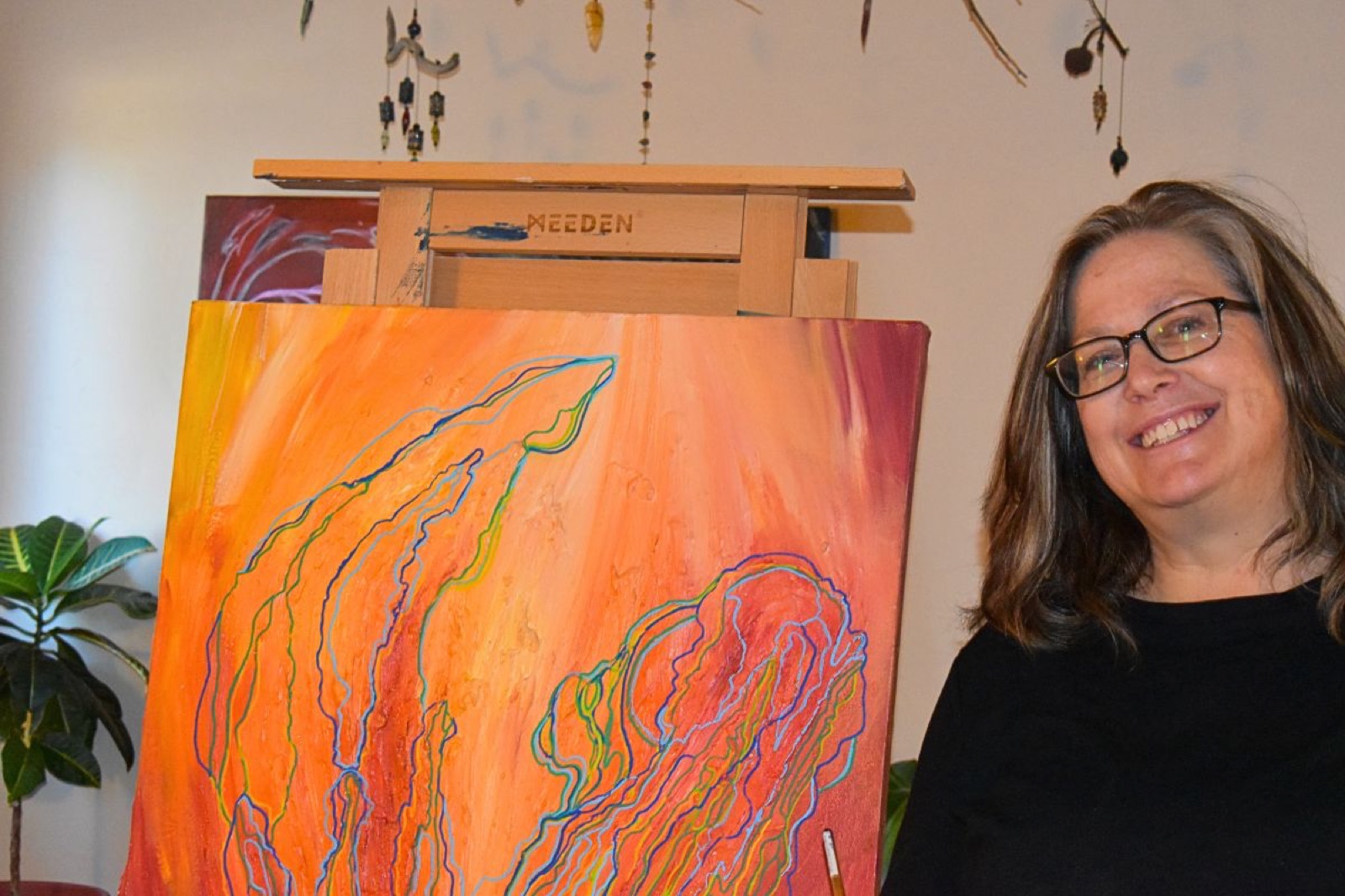 Diane Crenshaw smiling beside a large orange acrylic painting in her studio